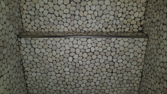 Flisearbejde med naturstensmosaik og integreret hylde i Spøttrup